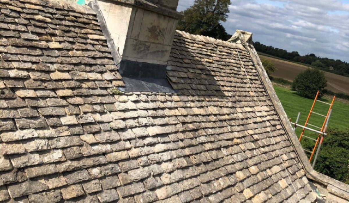 A house roof featuring a prominent chimney at its peak against a clear blue sky.  