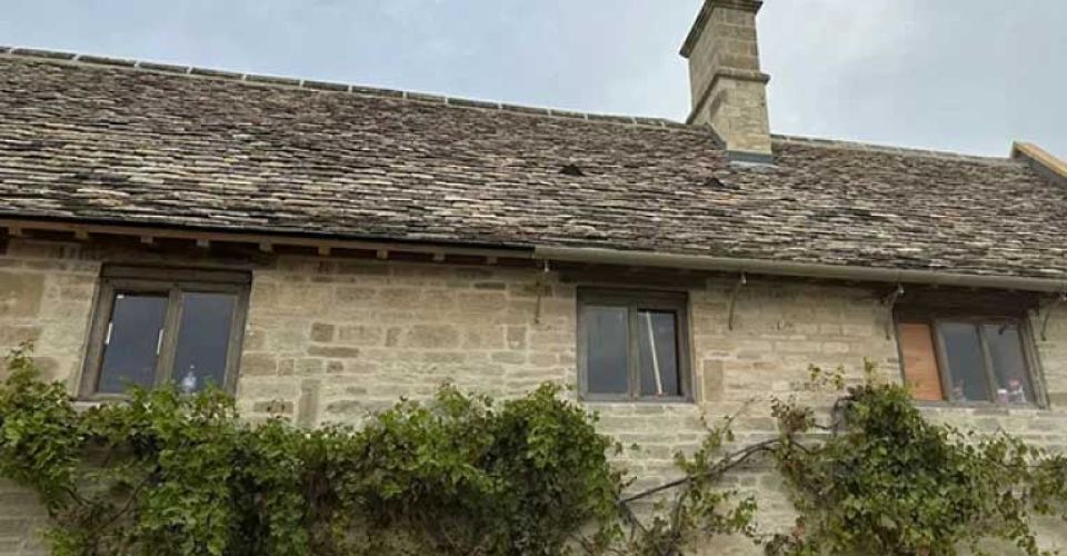 A stone house featuring a chimney and multiple windows against a clear sky. g